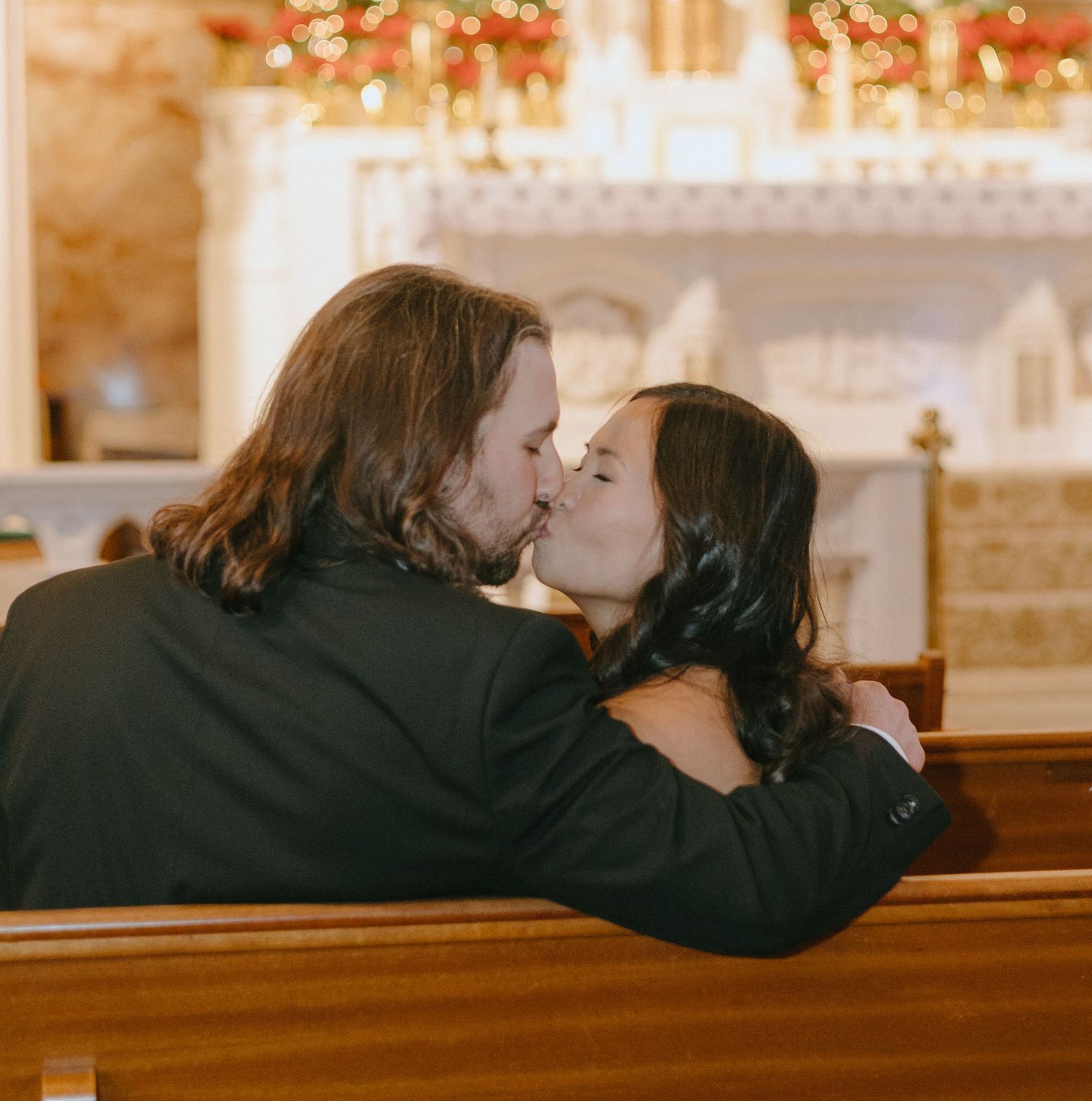 A romantic moment captured in church pews during a wedding ceremony.