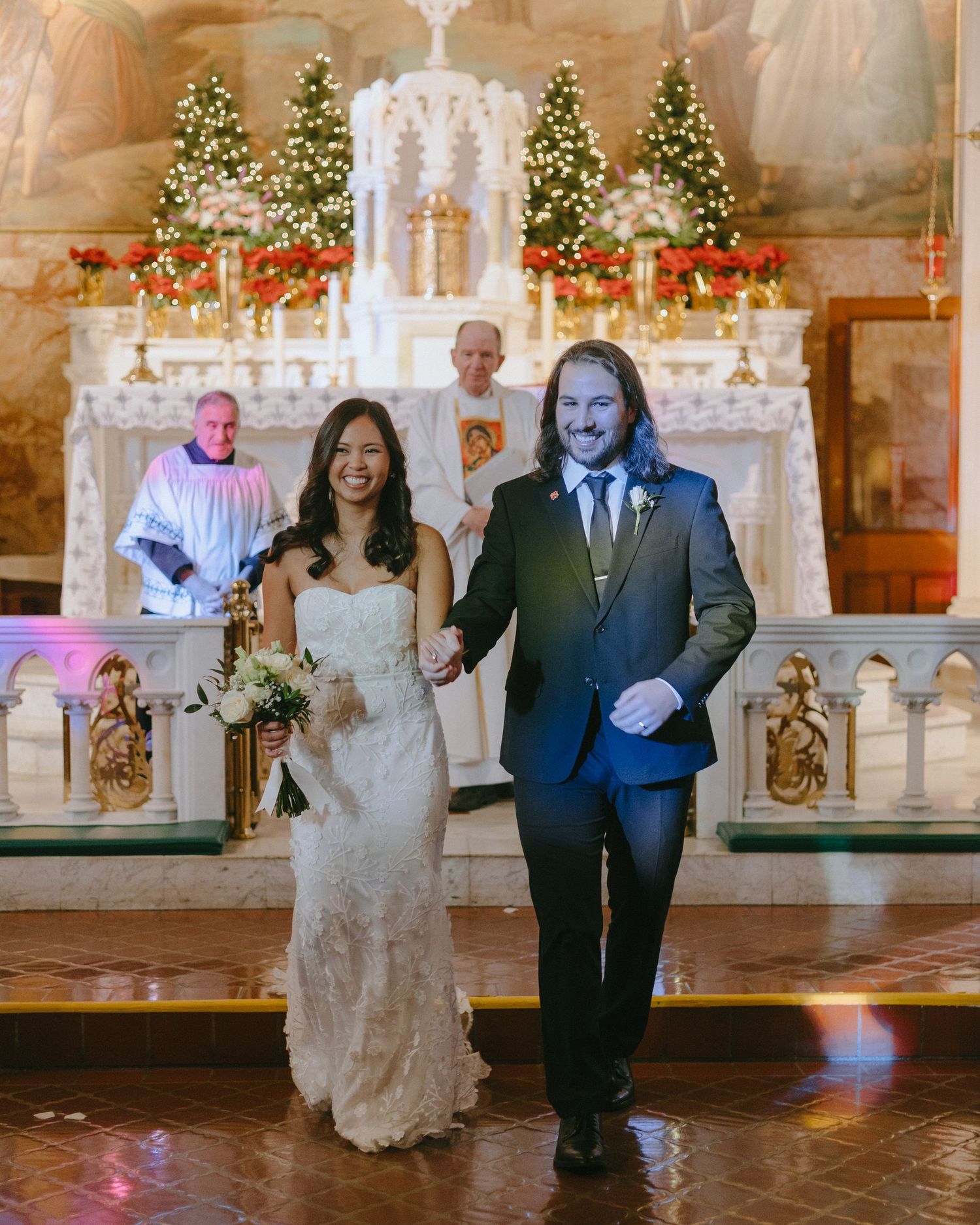 A wedding ceremony in a beautifully decorated church with Christmas trees and festive lighting.