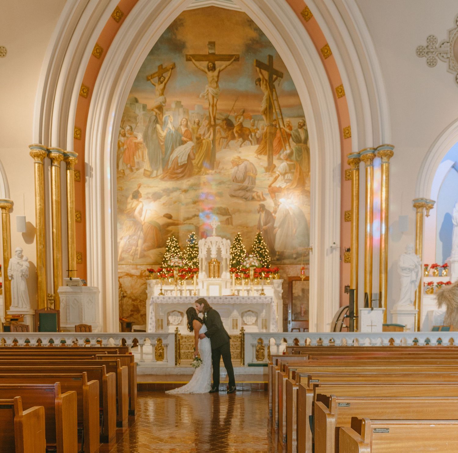 Wide view of church interior with arched ceilings, murals, and chandeliers during wedding ceremony.