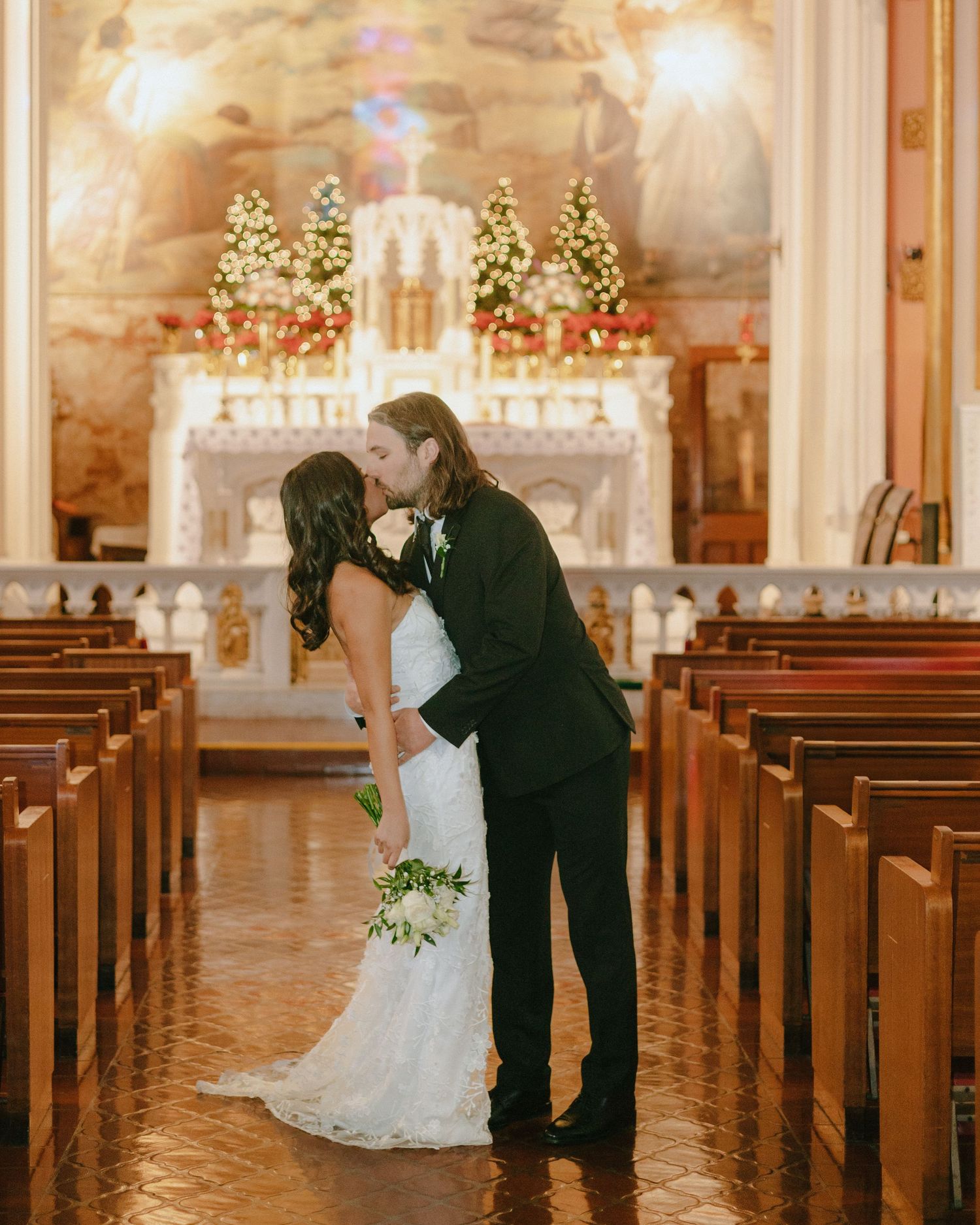 A wedding couple shares a moment in a beautifully decorated church with illuminated altar and pews.