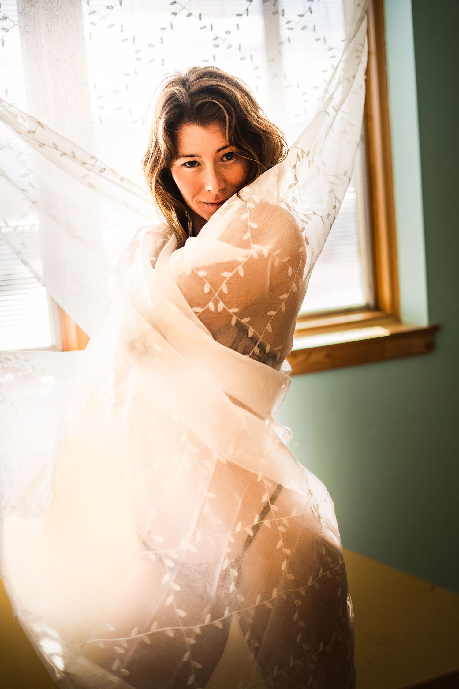Artistic boudoir photo sequence showing a figure draped in flowing white fabric against a sunlit window.