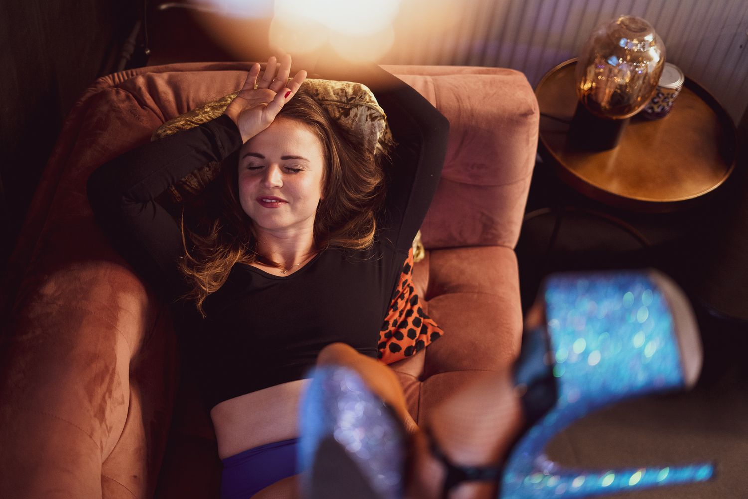 Someone relaxes on a brown leather couch with hair spread out while soft blue light illuminates the room.
