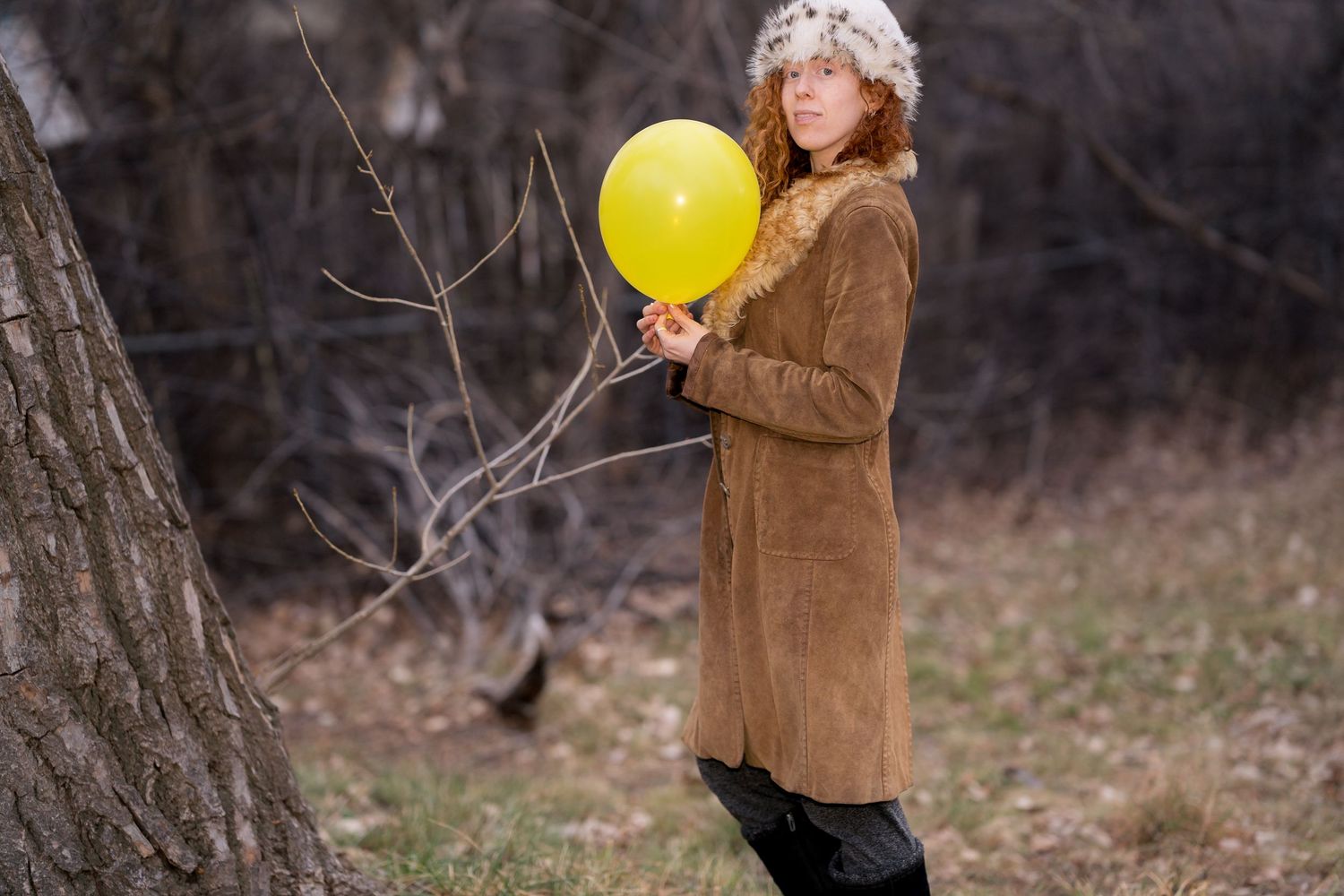 Person in brown coat holds yellow balloon outdoors in winter setting.