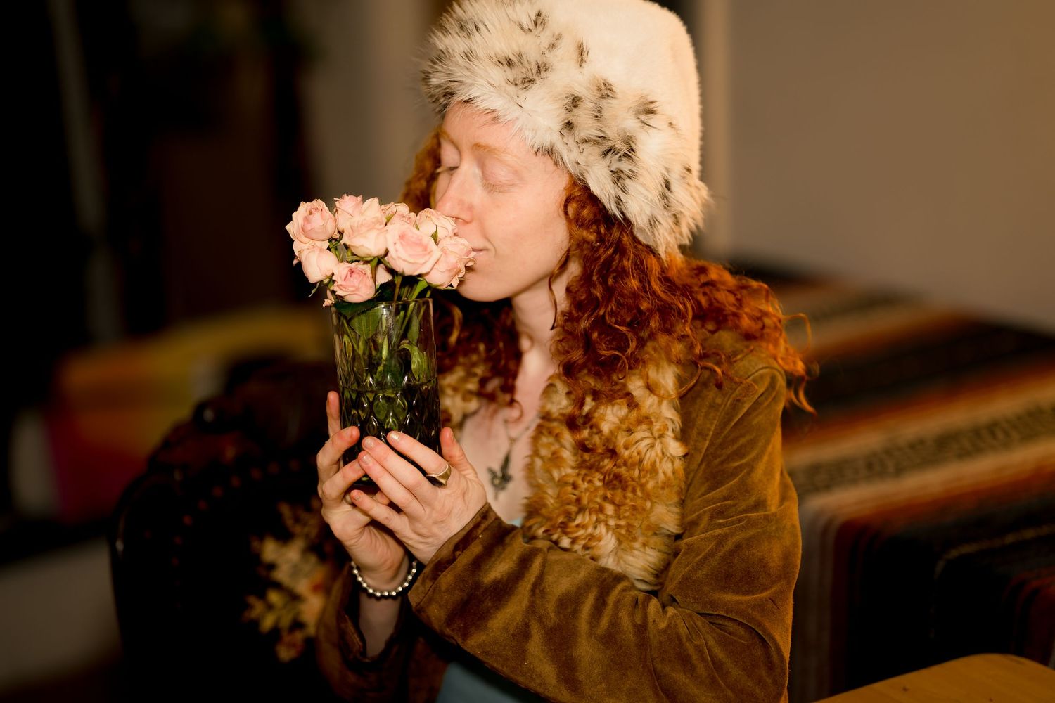 Person wearing lace bonnet and brown coat in warm indoor lighting.