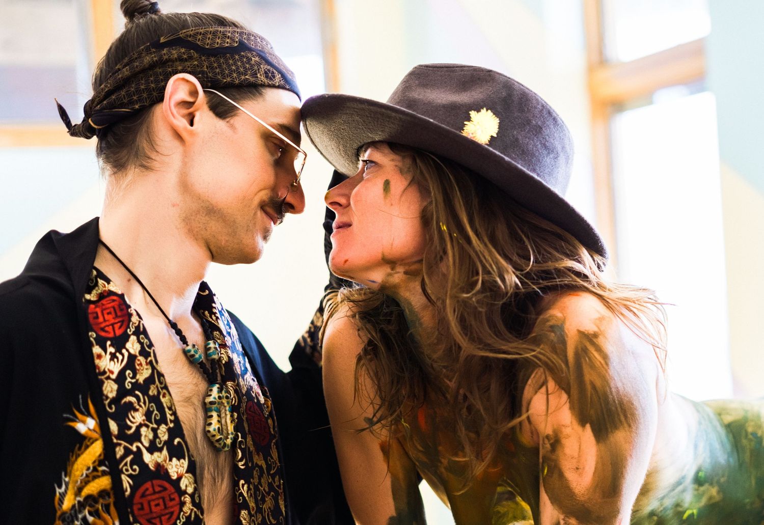 Stylish couple in vintage attire share a tender moment near a window.
