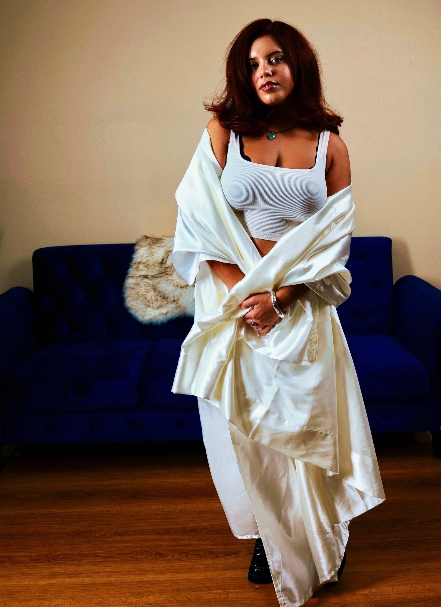 Elegant poses on hardwood floor with flowing white fabric and blue couch.