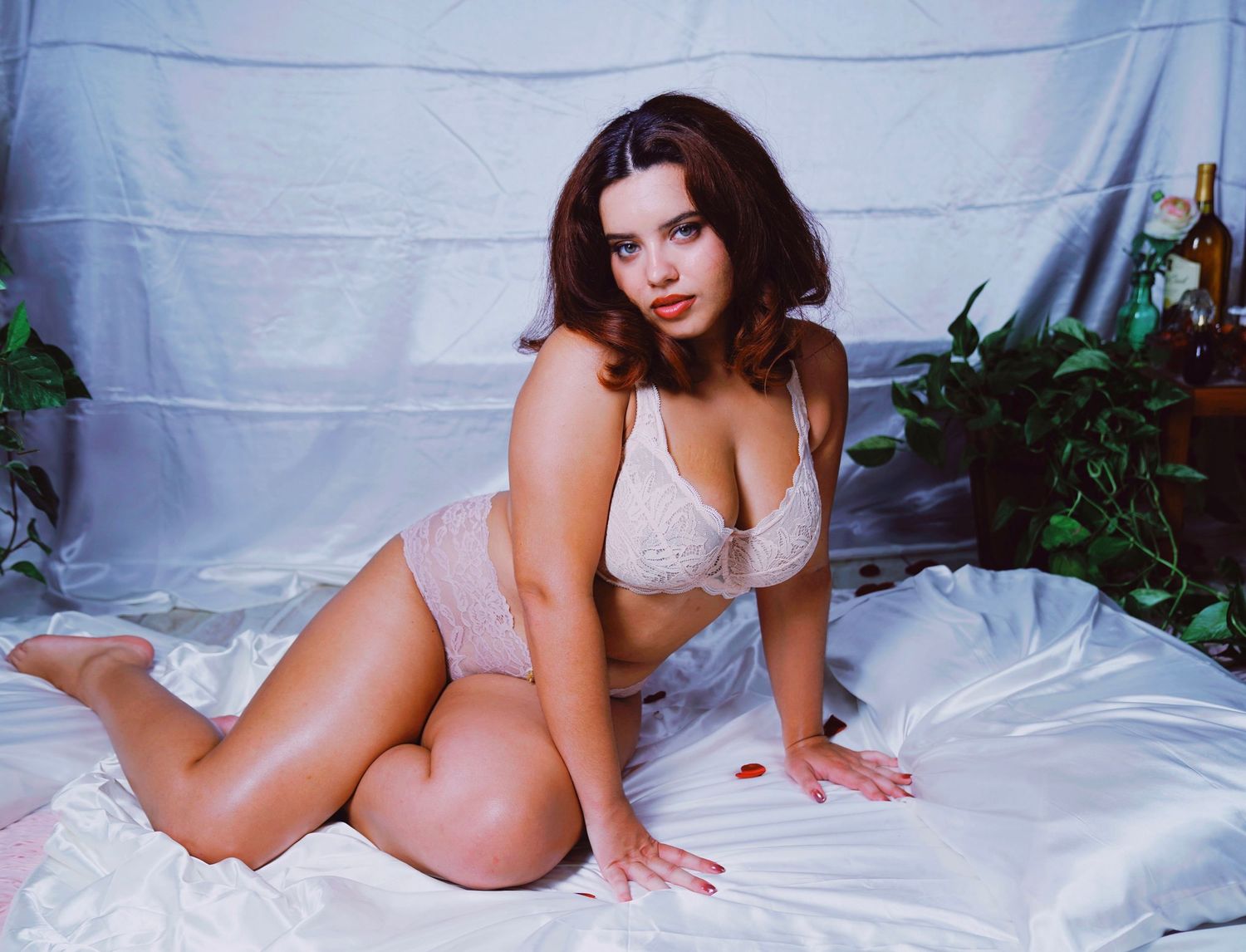 A figure in white lingerie poses seductively on white bedding in a boudoir photography series.
