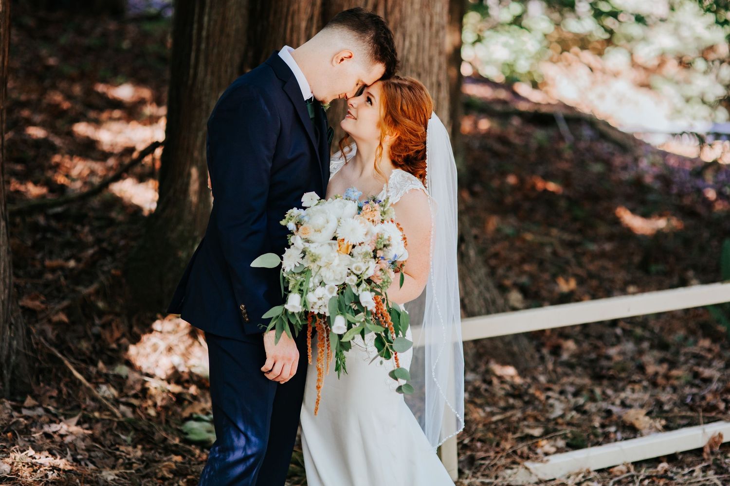 A couple in wedding attire holds hands and embraces in a romantic forest setting with dappled sunlight in Washington state