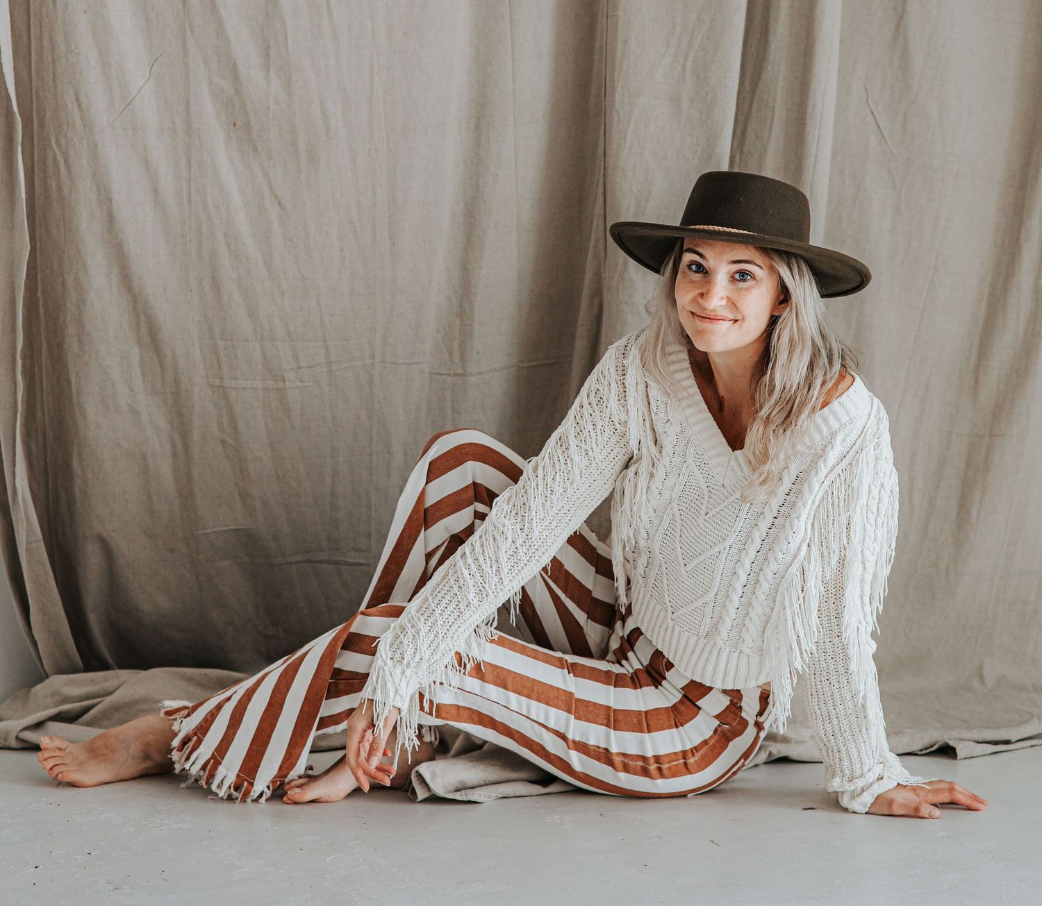 Cozy lifestyle photo featuring a white cable knit sweater and striped pants against a neutral backdrop in studio.