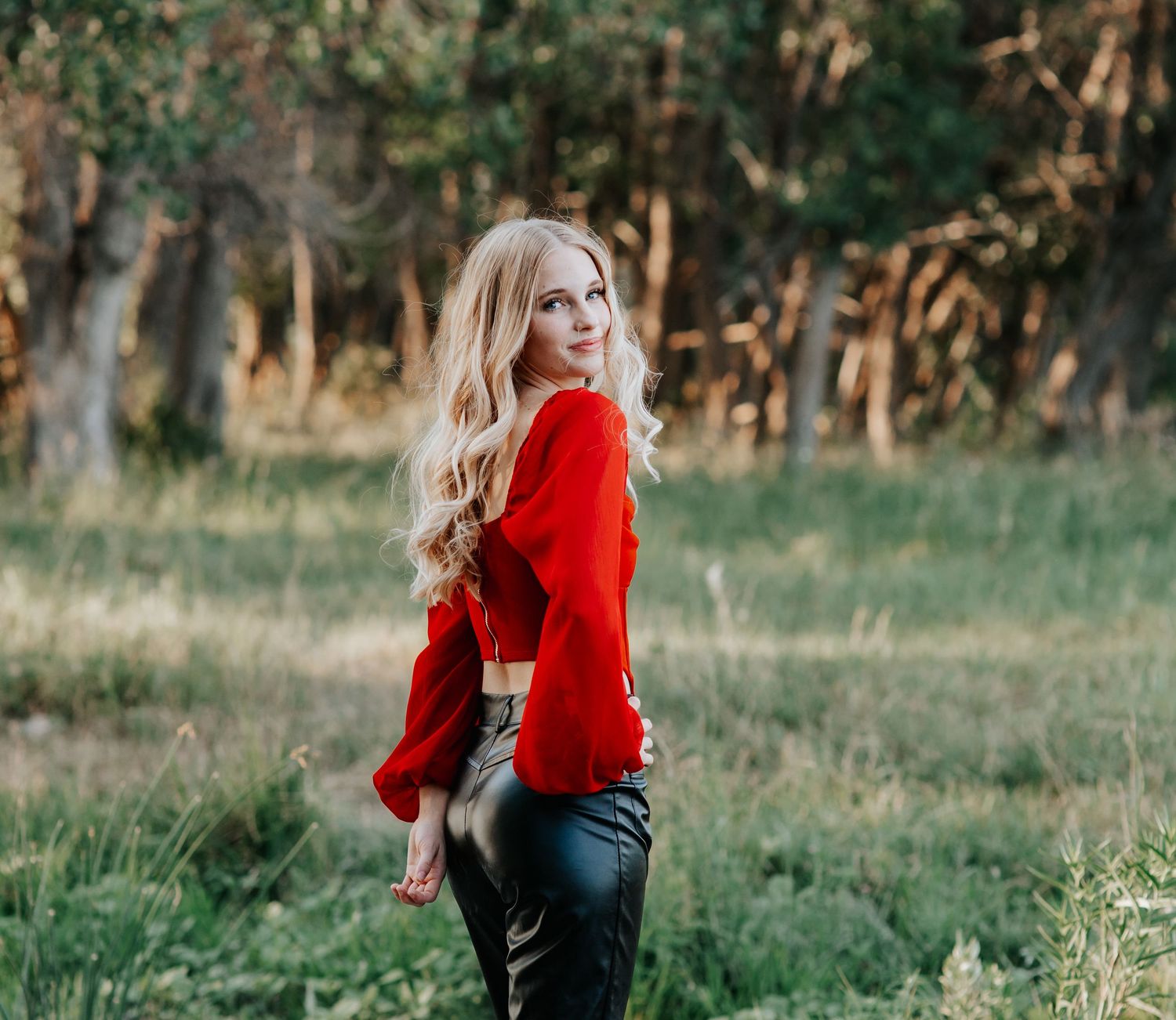 Senior session in a bright red sweater poses outdoors in an autumn setting in Kimball Nebraska.