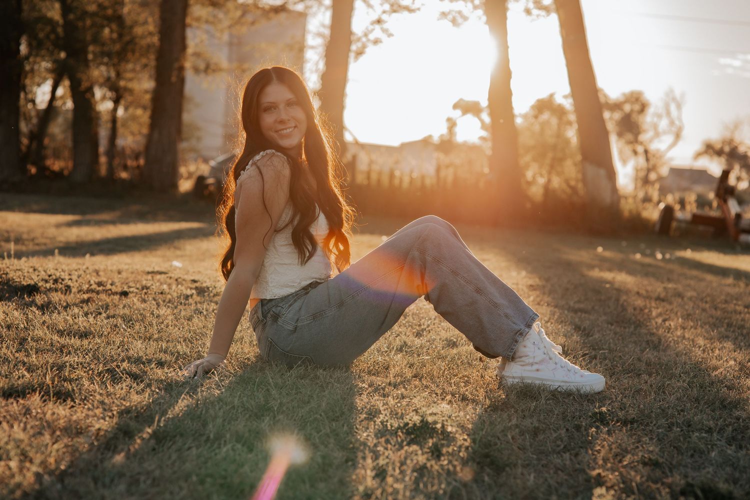 High School senior relaxing on grass at sunset wearing white sneakers and jeans in warm golden light in Bridgeport NE