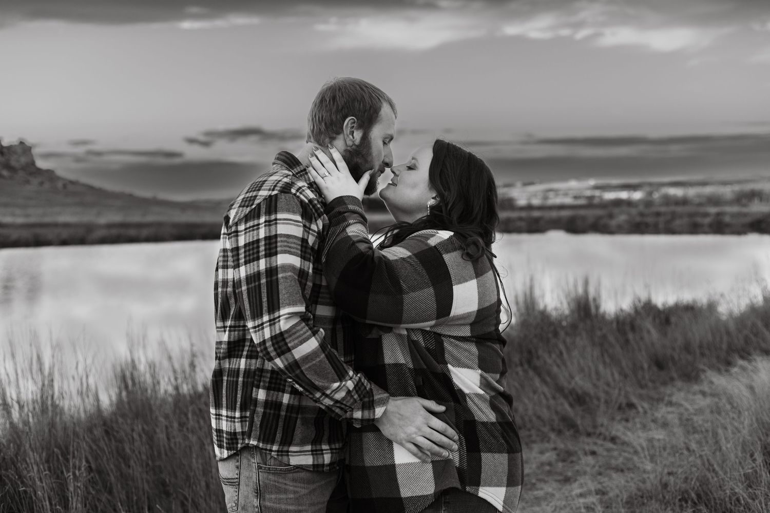 A black and white panoramic photo shows a couple in plaid embracing on a windswept coastal hillside.