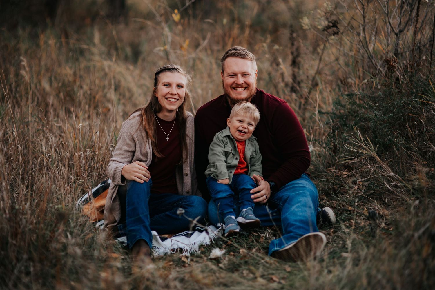 A family in coordinating blue outfits sits together in tall grass during an outdoor fall photoshoot in the Black Hills of South Dakota.