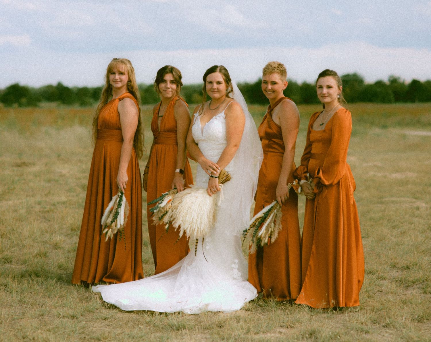 Wedding party in burnt orange bridesmaid dresses poses together in an outdoor field setting in Bridgeport Nebraska.