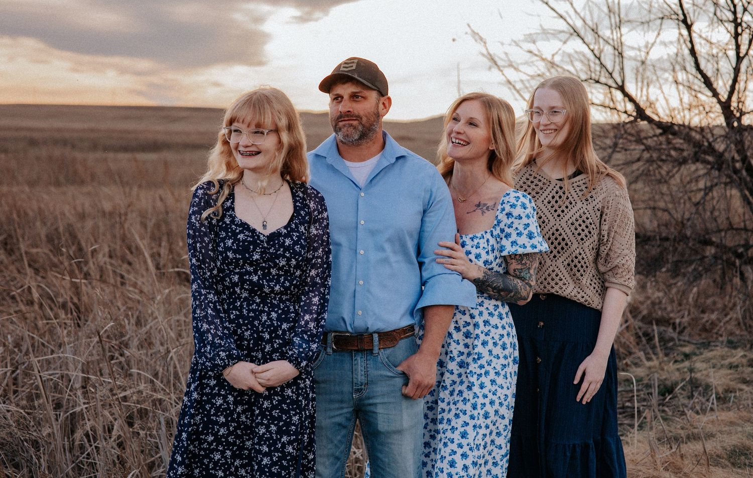 Family of four posing outdoors at sunset in a field, wearing casual attire, smiling together.