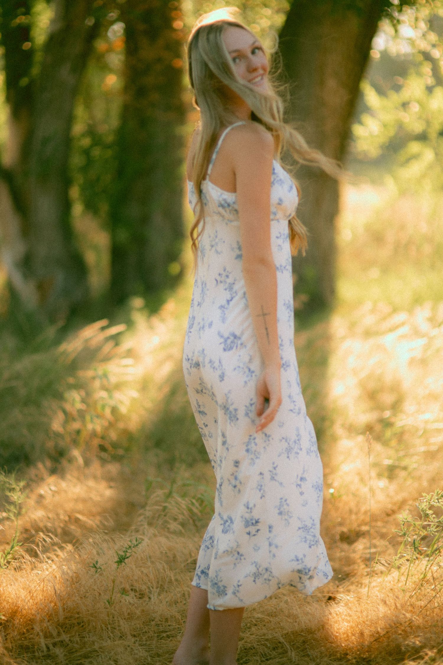 A dreamy summer scene shows a white floral dress swaying in golden sunlight filtering through trees for a senior session in Nebraska