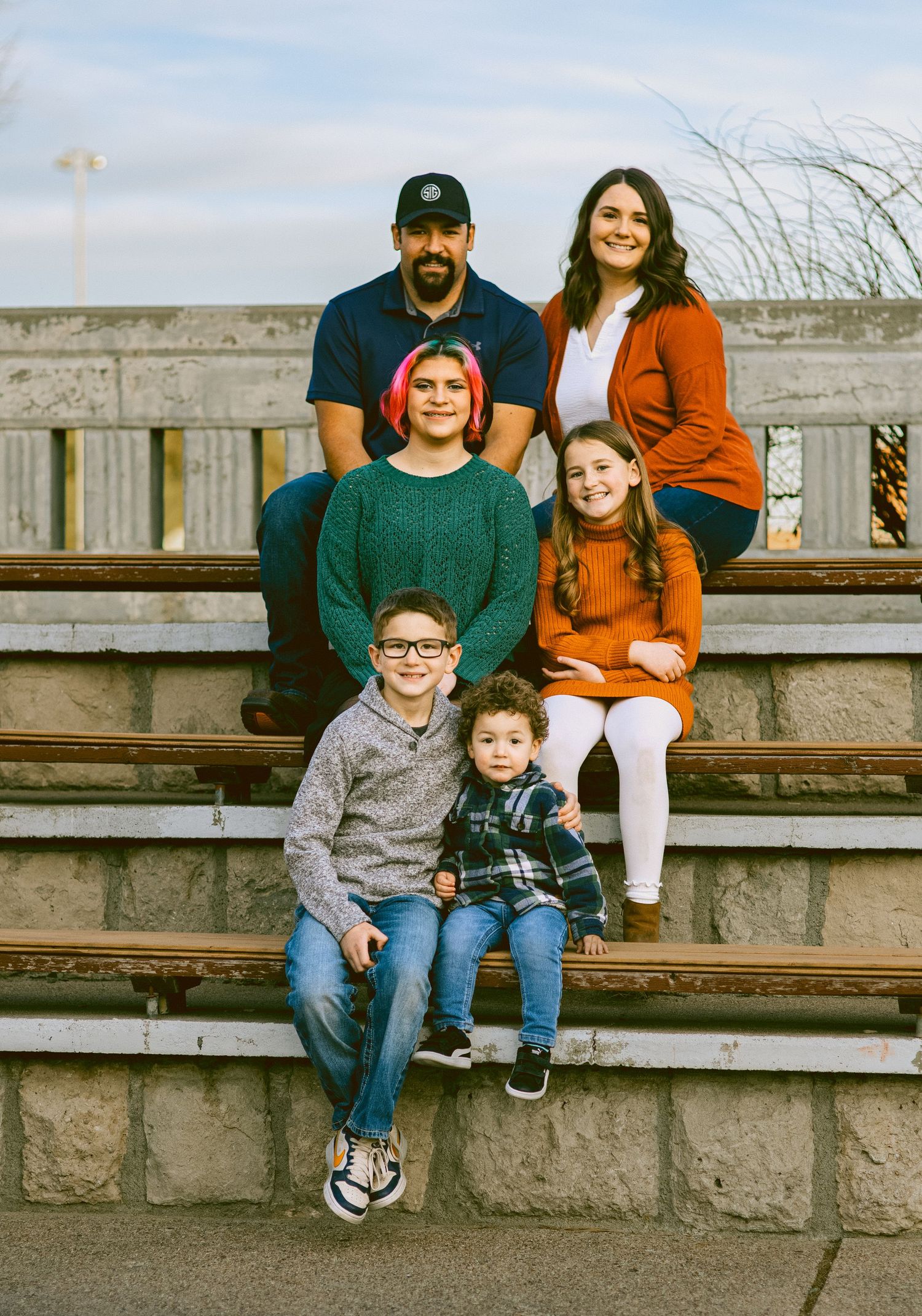 Family of six sitting together on outdoor stone steps in casual attire during a portrait session.