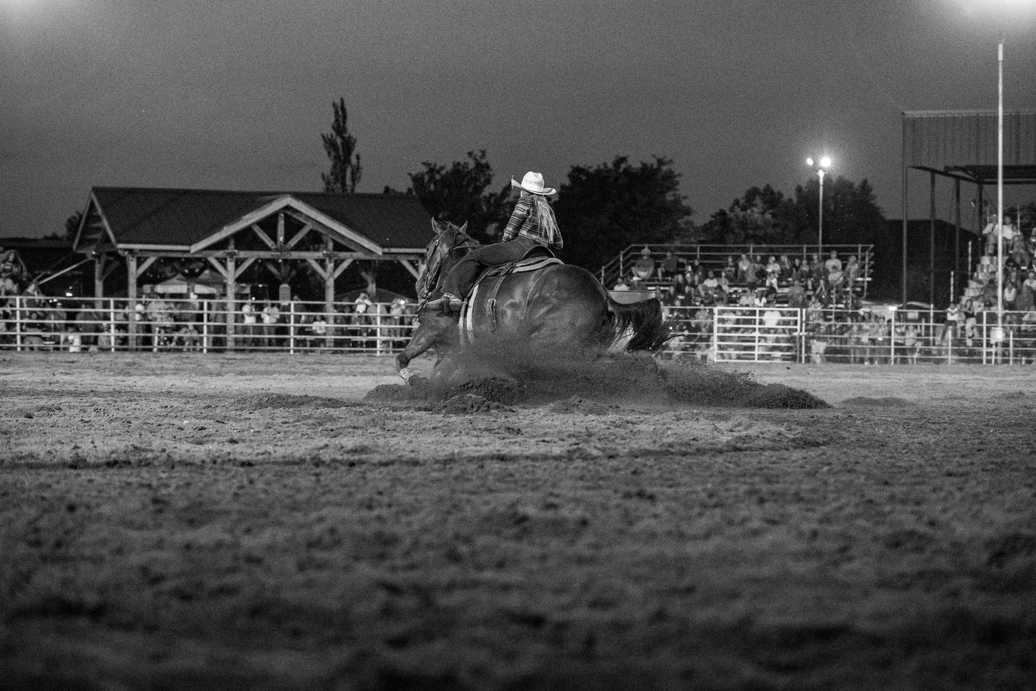 A dramatic black and white rodeo scene shows a rider on horseback kicking up dust during a nighttime performance in Nebraska