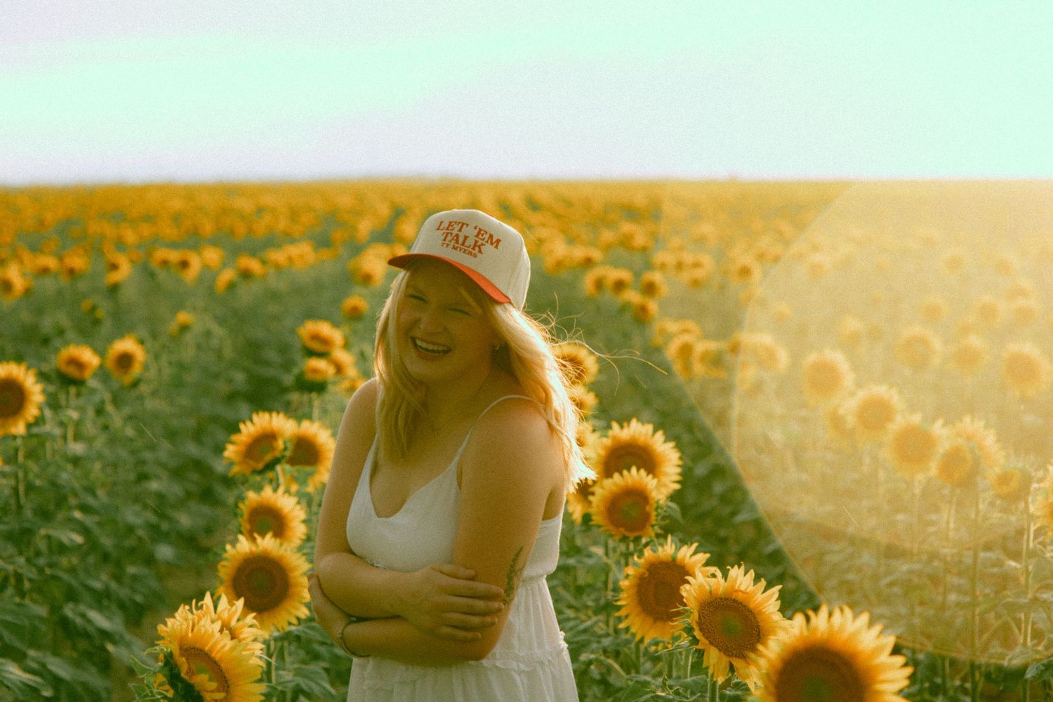 A golden sunflower field glows warmly during sunset with a figure silhouetted against the vibrant orange sky during a senior session in NE