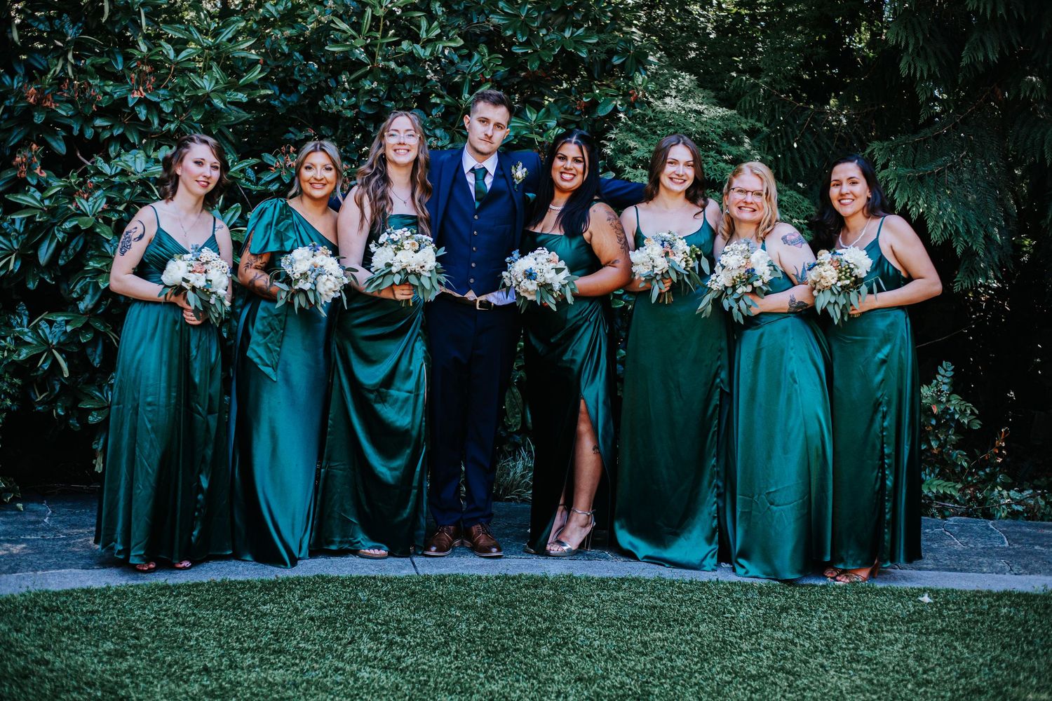 Wedding party in emerald green dresses poses casually on grass during outdoor wedding in Washington.