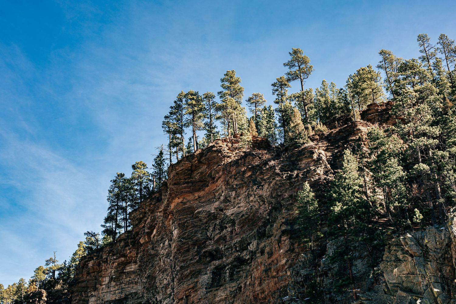 A scenic mountain landscape with rocky cliffs and evergreen trees against a bright blue sky in Spearfish SD