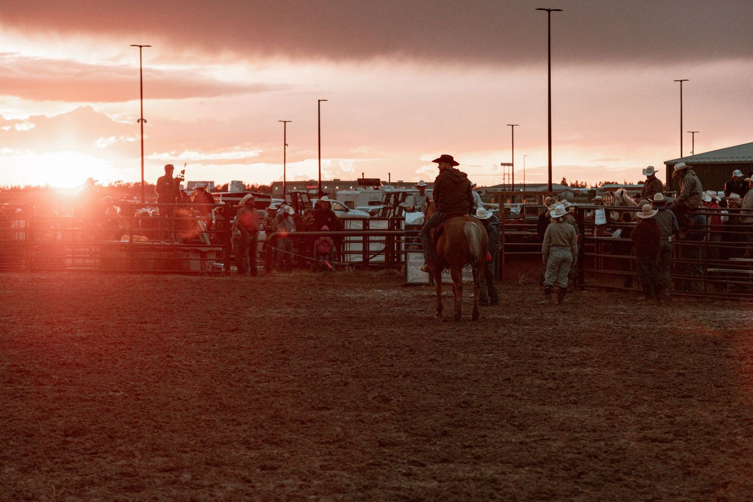 Panoramic view of a rodeo arena at sunset with riders silhouetted against an orange sky.