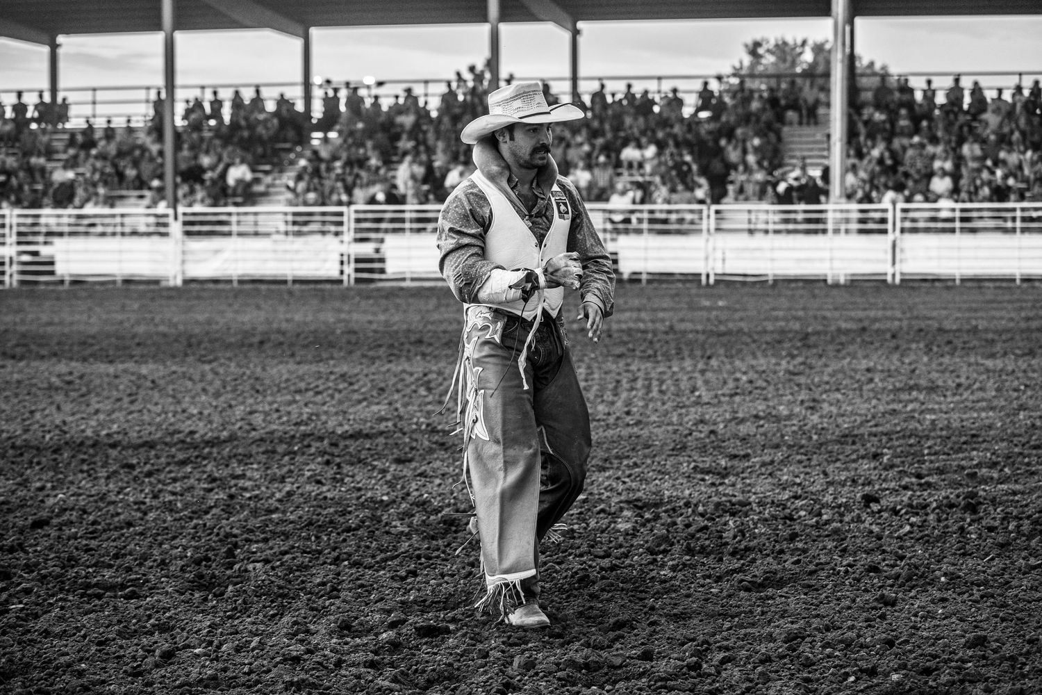 Wide shot of cowboys competing in a rodeo arena with spectators in the grandstands.