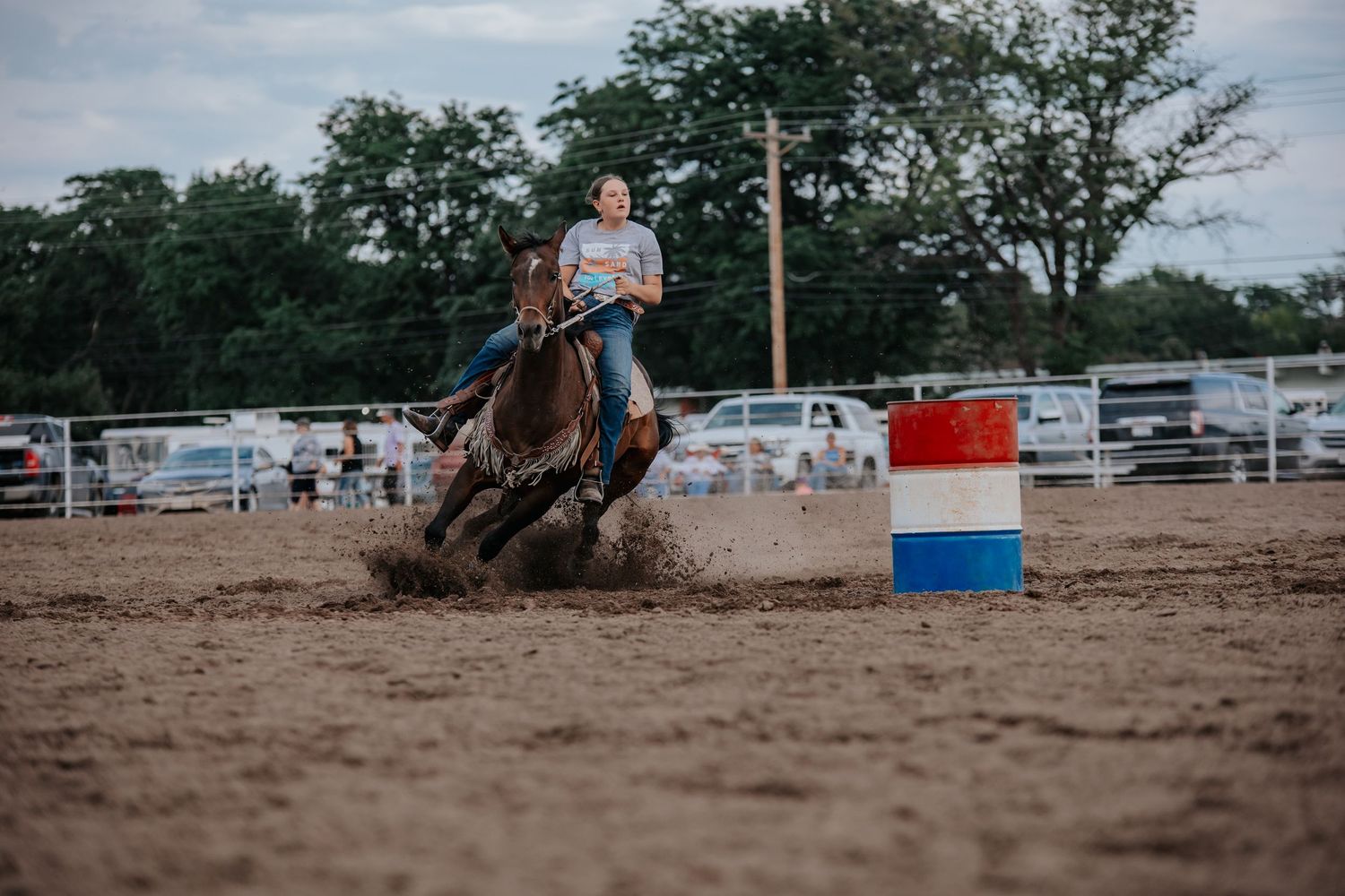 Barrel racing competition at a rodeo event showing horse and rider navigating around barrels on a dirt arena in Kimball, Nebraska