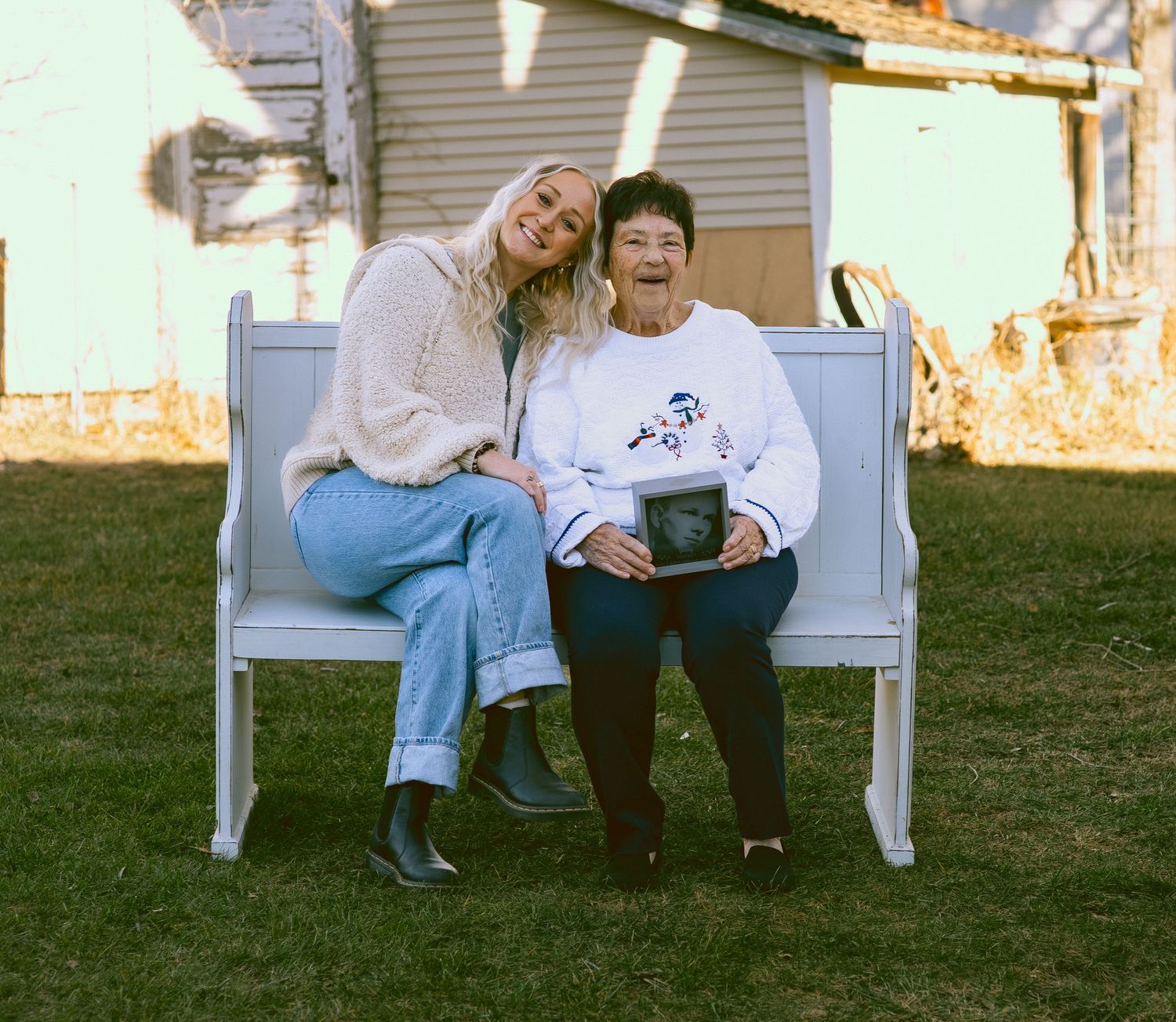 Two people sitting together on a white wooden bench in a backyard with casual attire and relaxed poses.