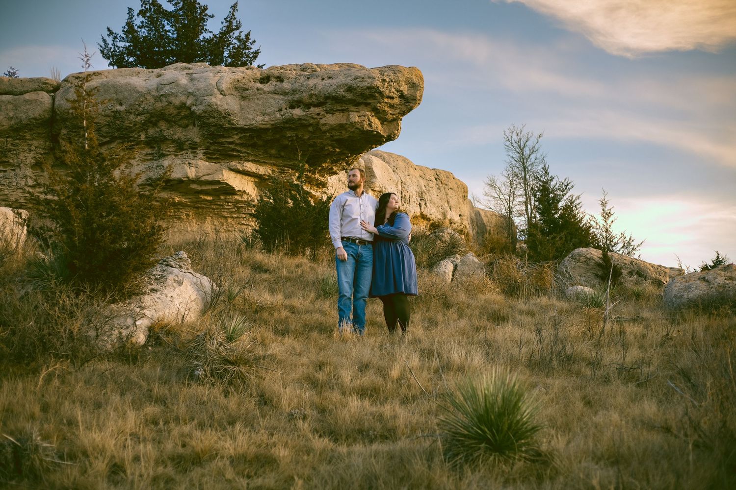 A engaged couple stands together against a scenic rocky landscape during golden hour in Sidney Nebraska.