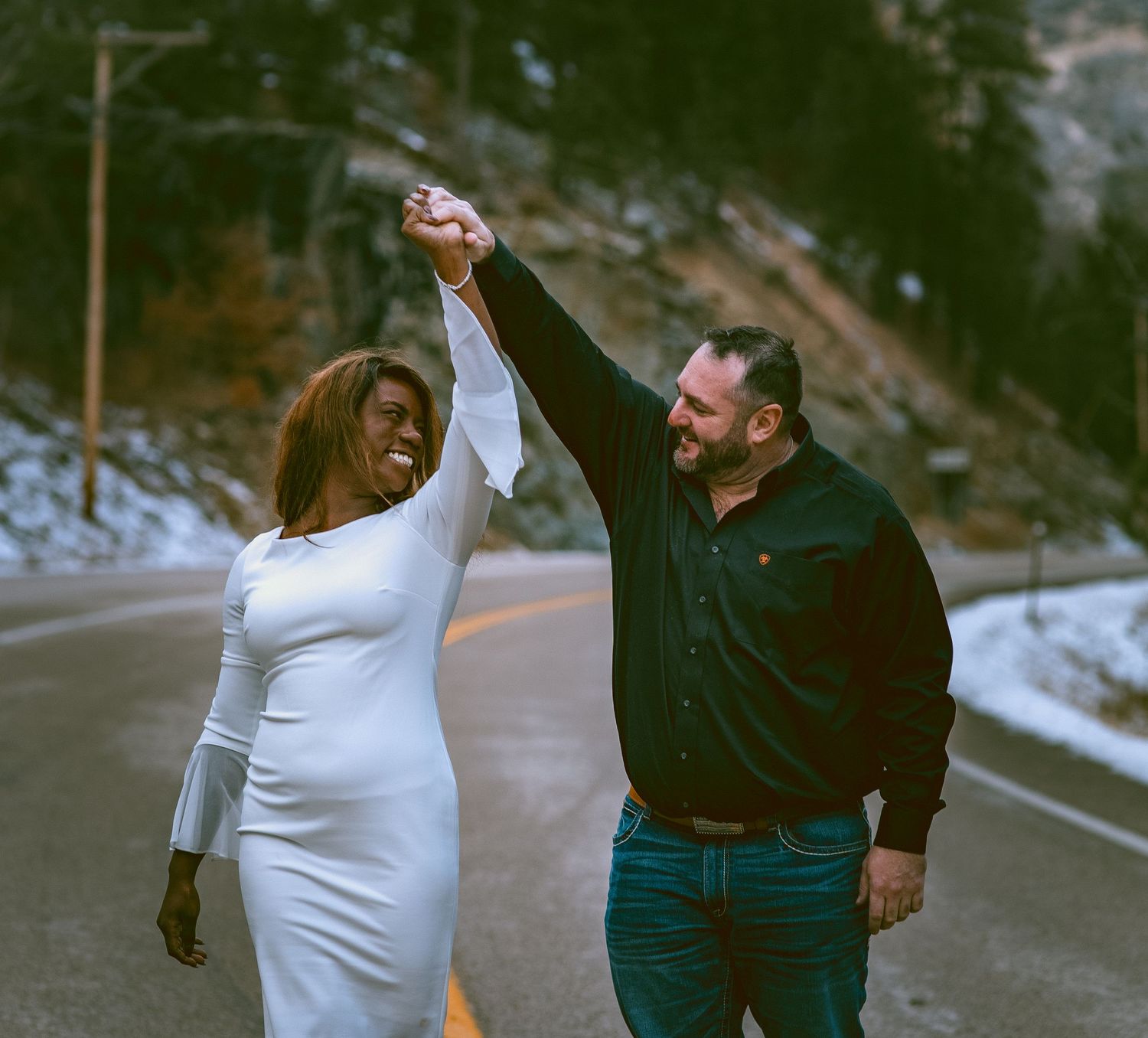 A engaged couple holding hands and walking together on a snowy mountain road in winter in Spearfish South Dakota.