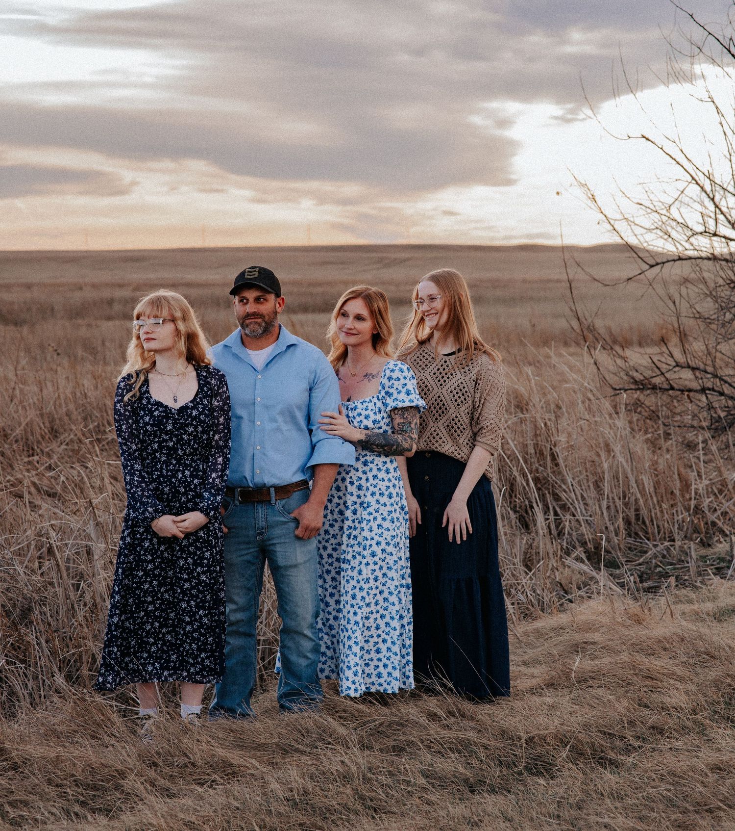 Family of four posing together in a golden prairie field at sunset, wearing casual and elegant attire.
