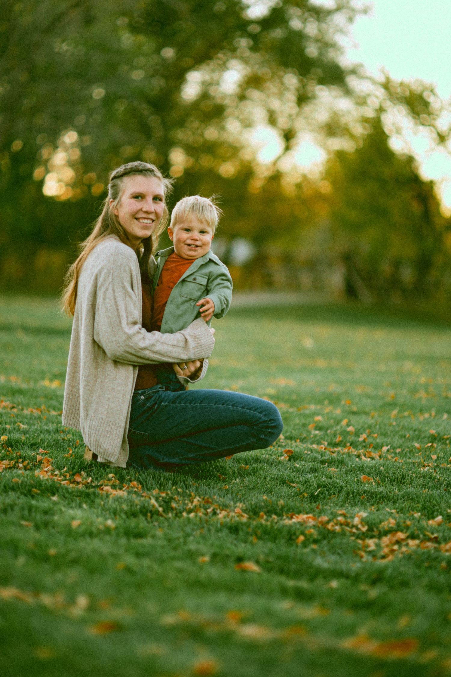 Family relaxing together on a grassy hill during autumn sunset.