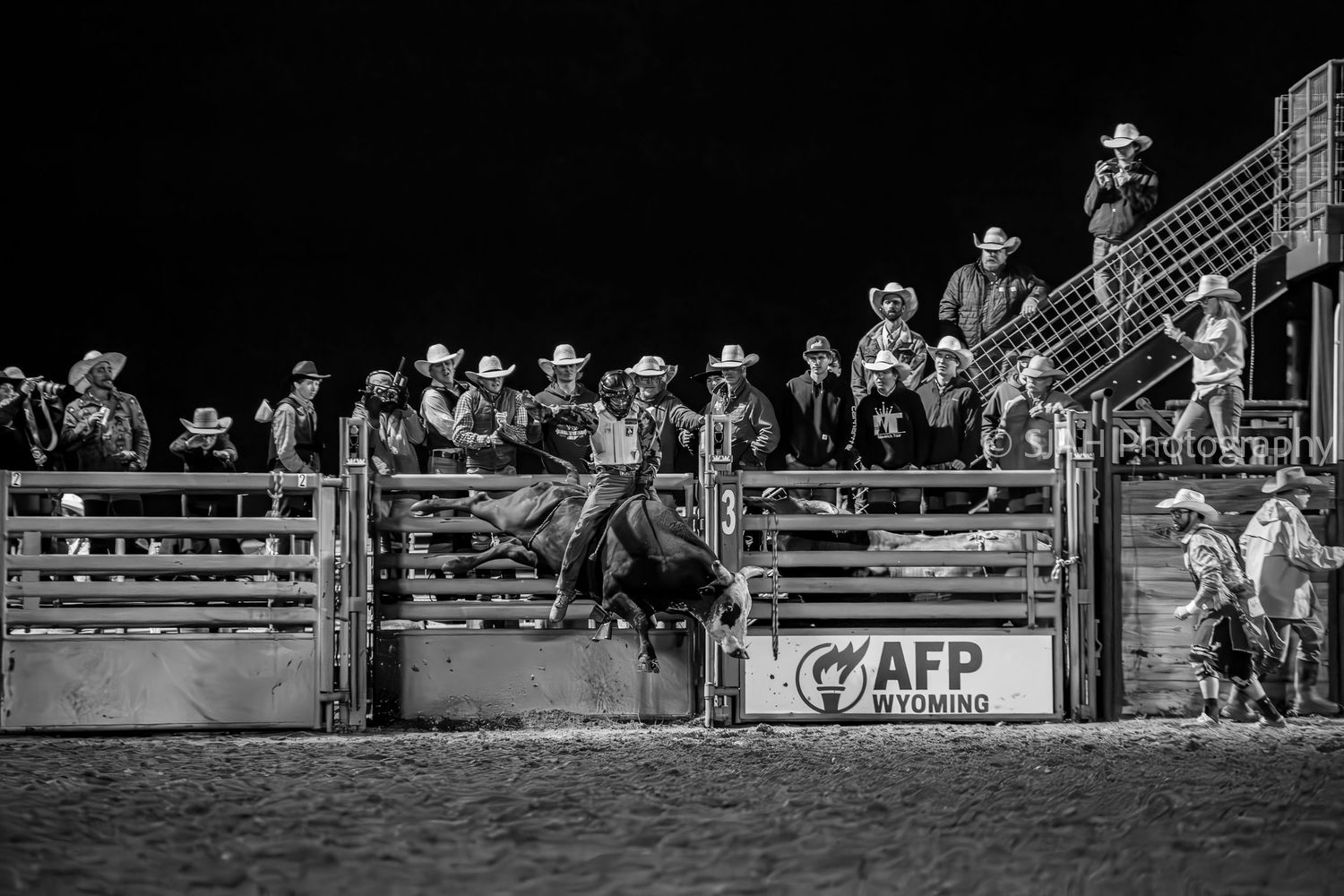 Monochrome image of rodeo spectators lined up along arena fencing during an event in Cheyenne Wyoming.