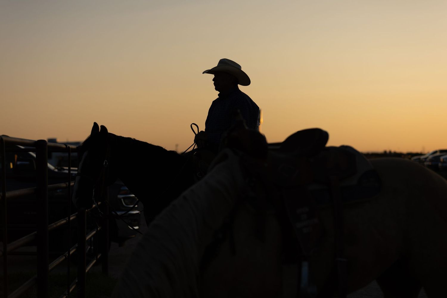 Silhouetted cowboys and horses against a sunset sky at a rodeo arena in Cheyenne Wyoming.