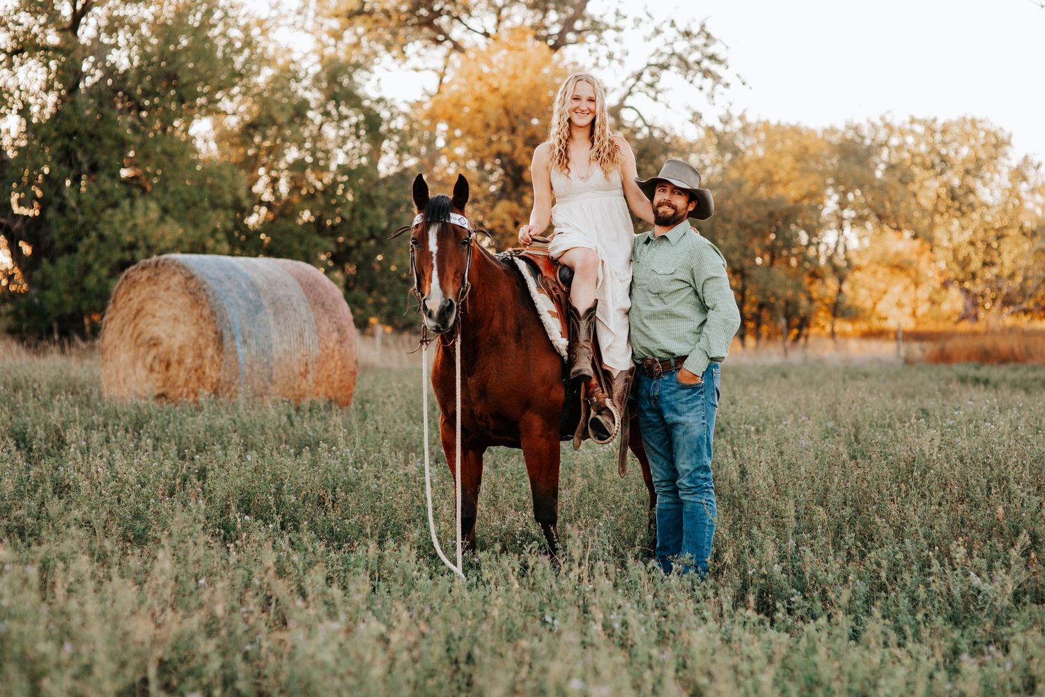 Couple poses with horses in a golden sunset field during autumn in Harrison Nebraska.