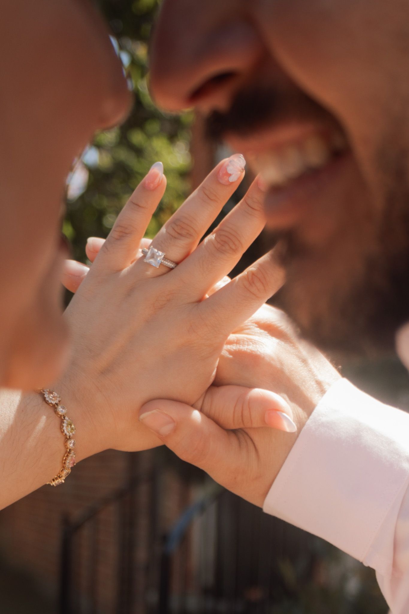 Couple kissing while showing off a diamond engagement ring and gold bracelet on her hand.