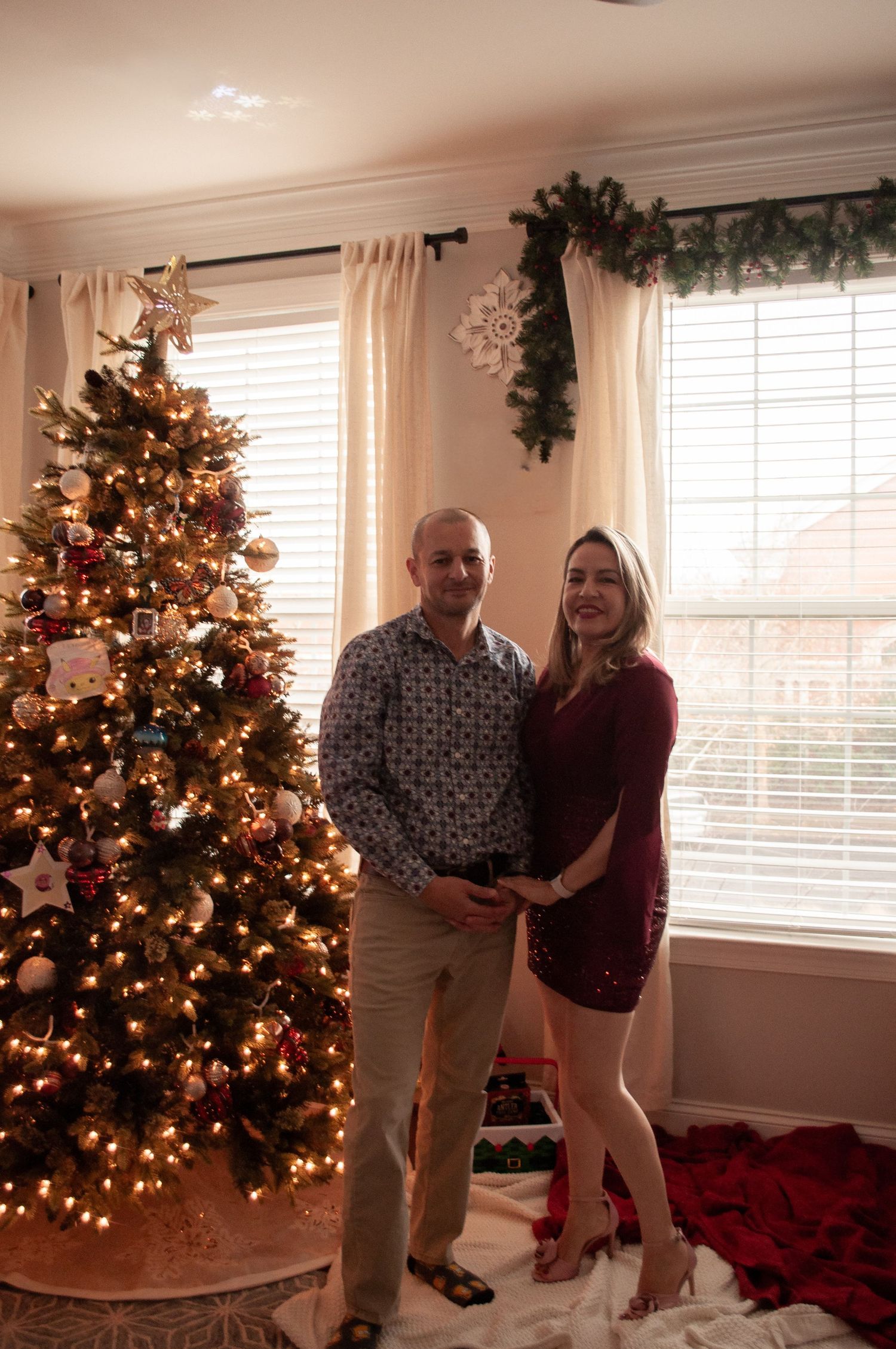 Couple smiling together beside a decorated Christmas tree with warm lights in a festive holiday living room.