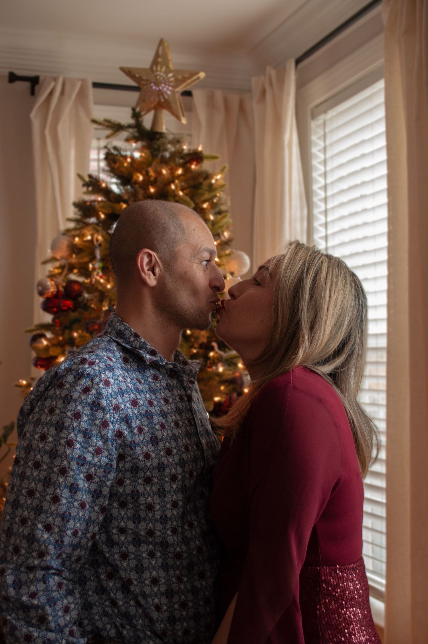 Couple sharing a romantic kiss in front of a decorated Christmas tree with glowing lights and a star topper.