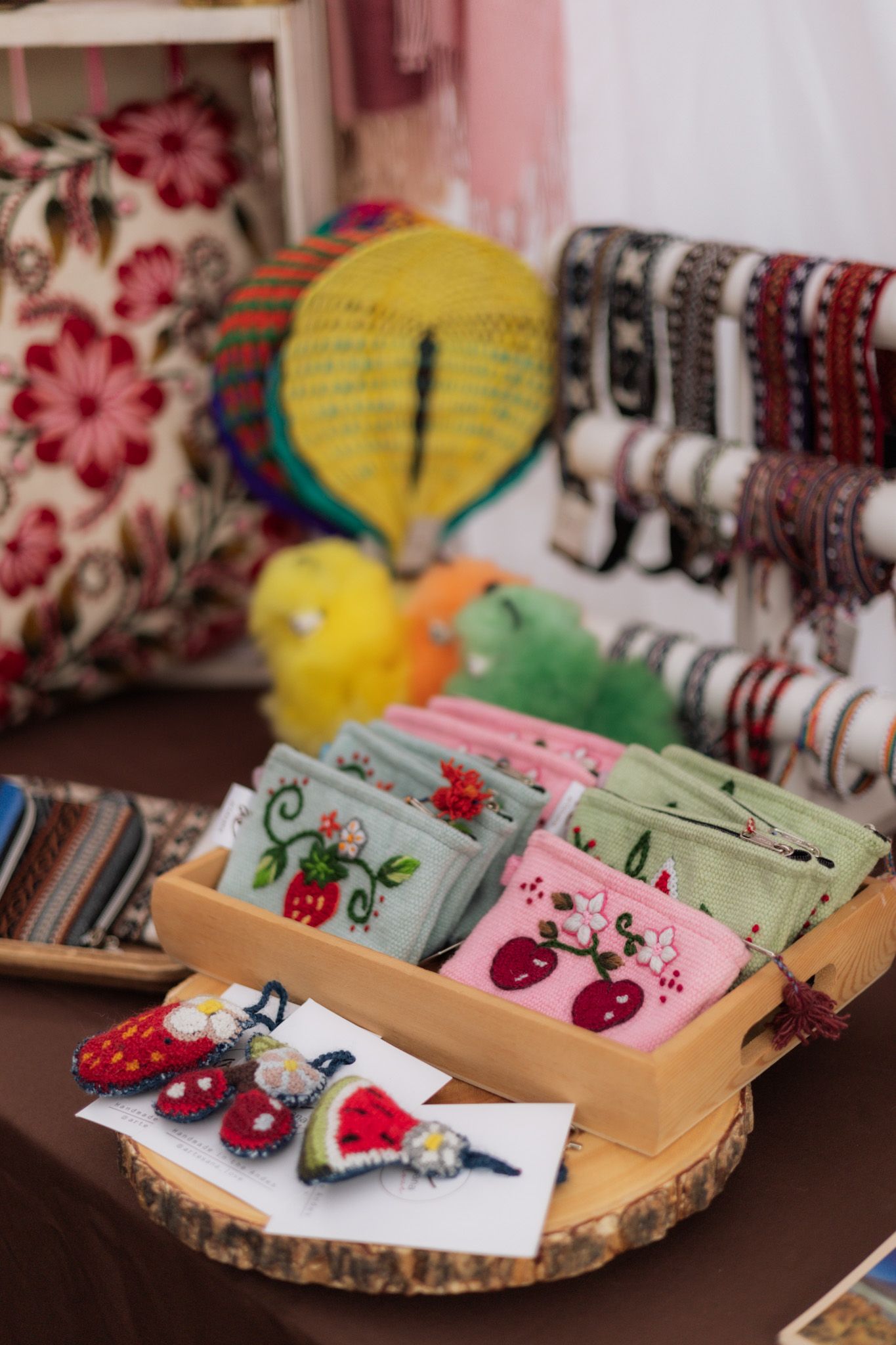 Colorful handmade crafts display with embroidered wallets, felt brooches, bracelets, and decorative items at an artisan market.