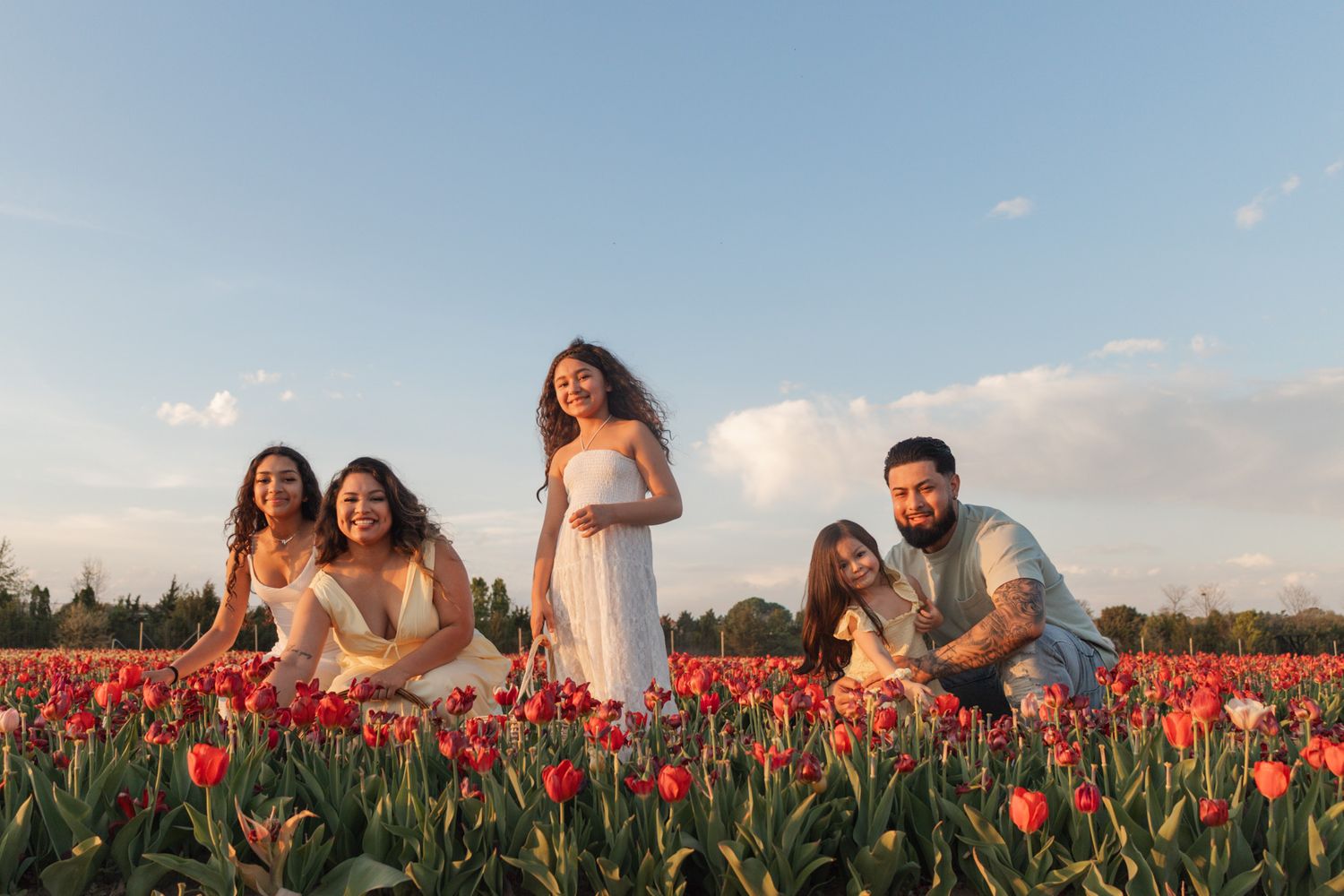 Family of 5 posing happily in a vibrant red tulip field under a blue sky at golden hour.