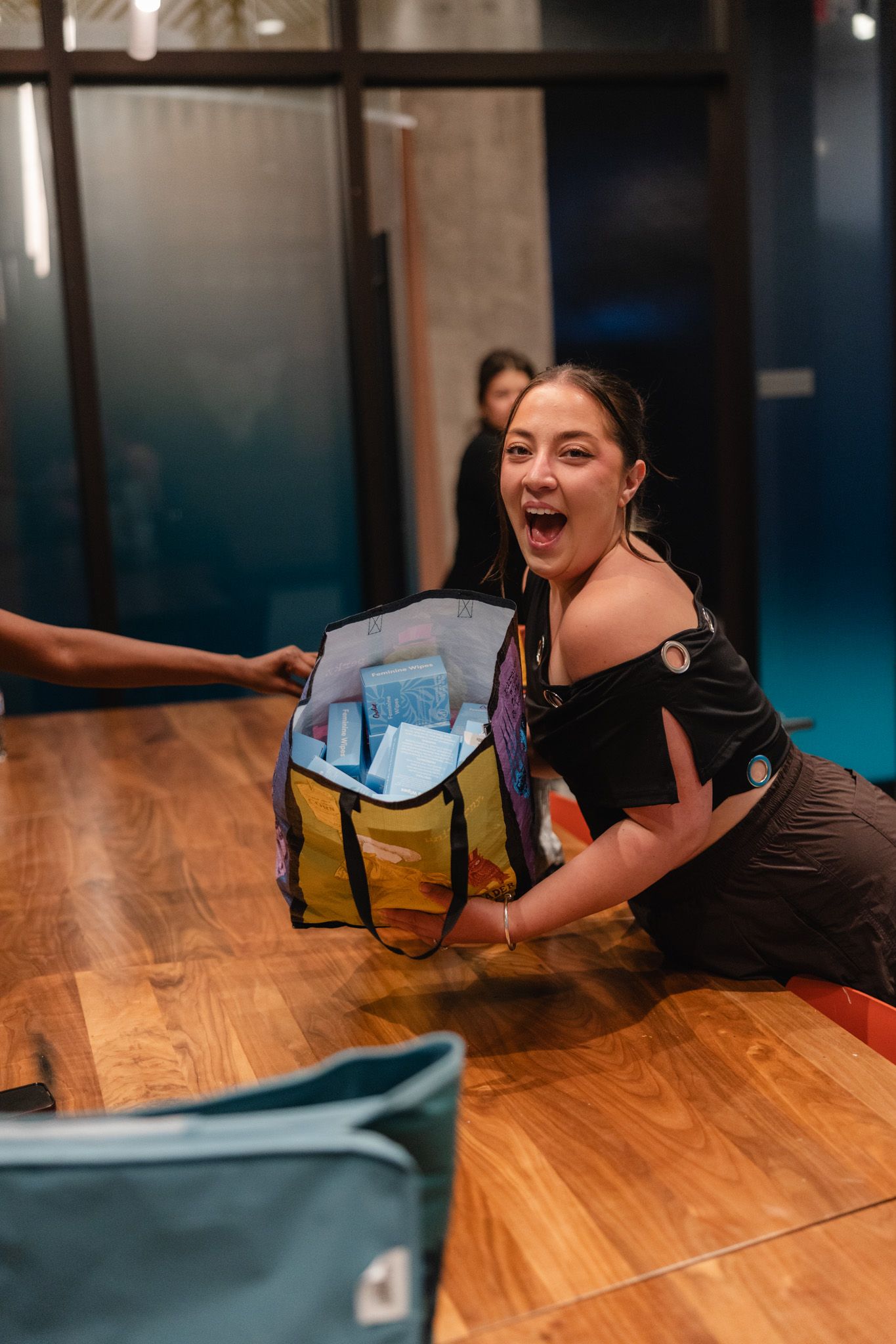 Excited woman receiving a colorful insulated bag filled with items at a wooden counter indoors.