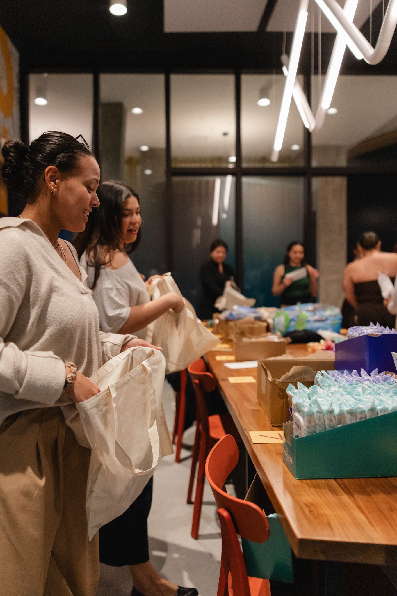 Women browsing gift bags and products at an indoor event table with colorful packaging displays.