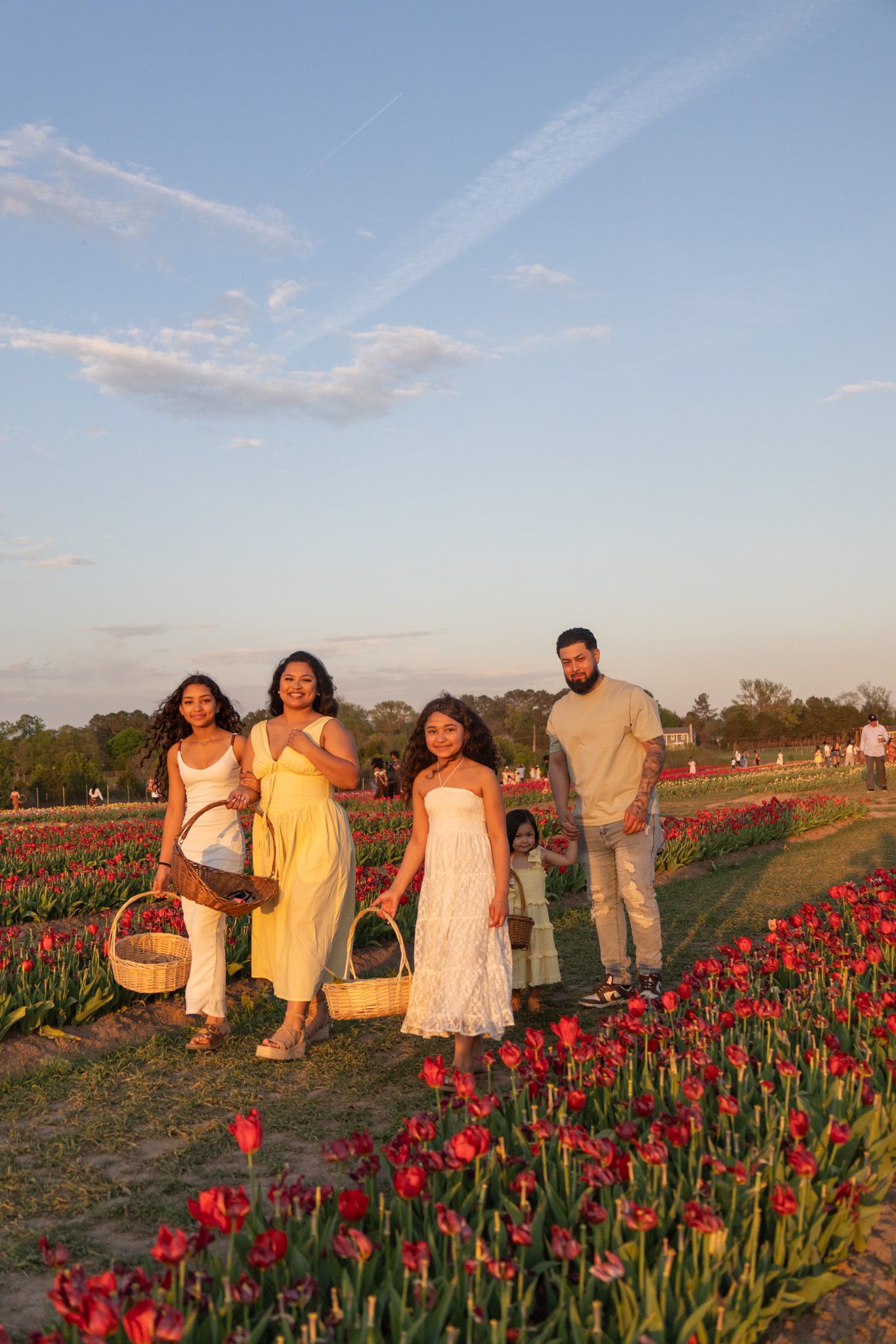 Family posing in a tulip field at golden hour, with women holding baskets and children nearby.