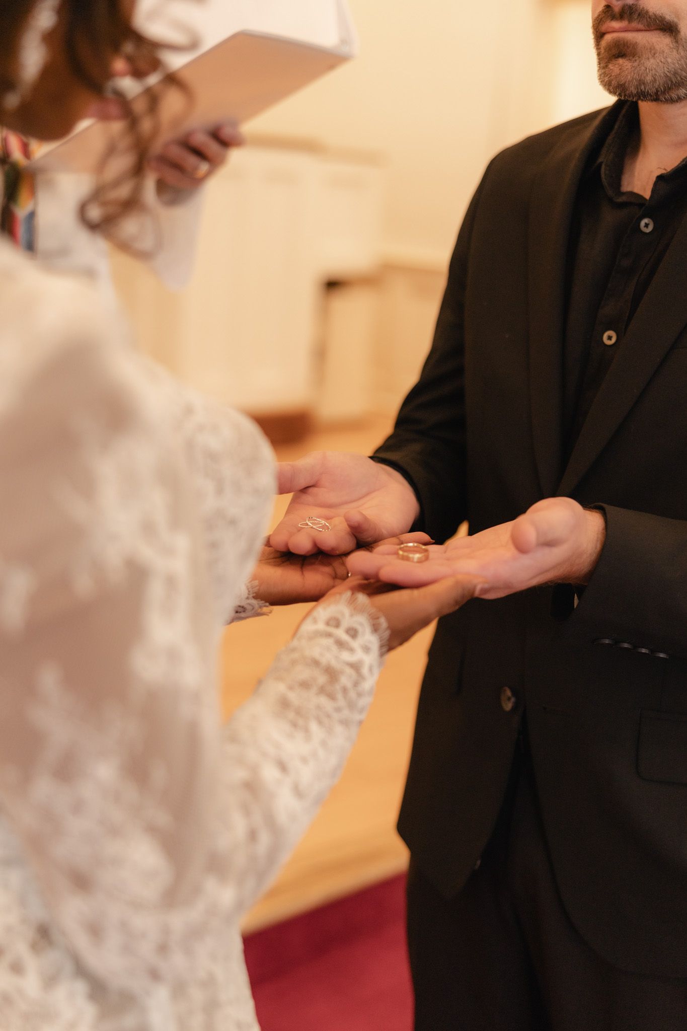 Bride in lace dress placing a gold wedding ring on groom's finger during church ceremony.