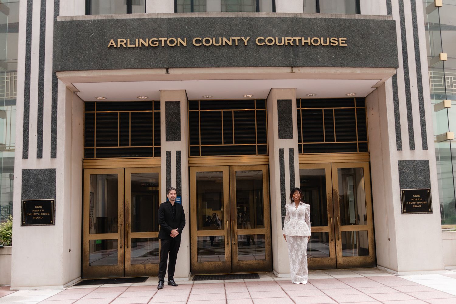 Couple posing outside Arlington County Courthouse entrance with gold doors after their courthouse wedding ceremony.
