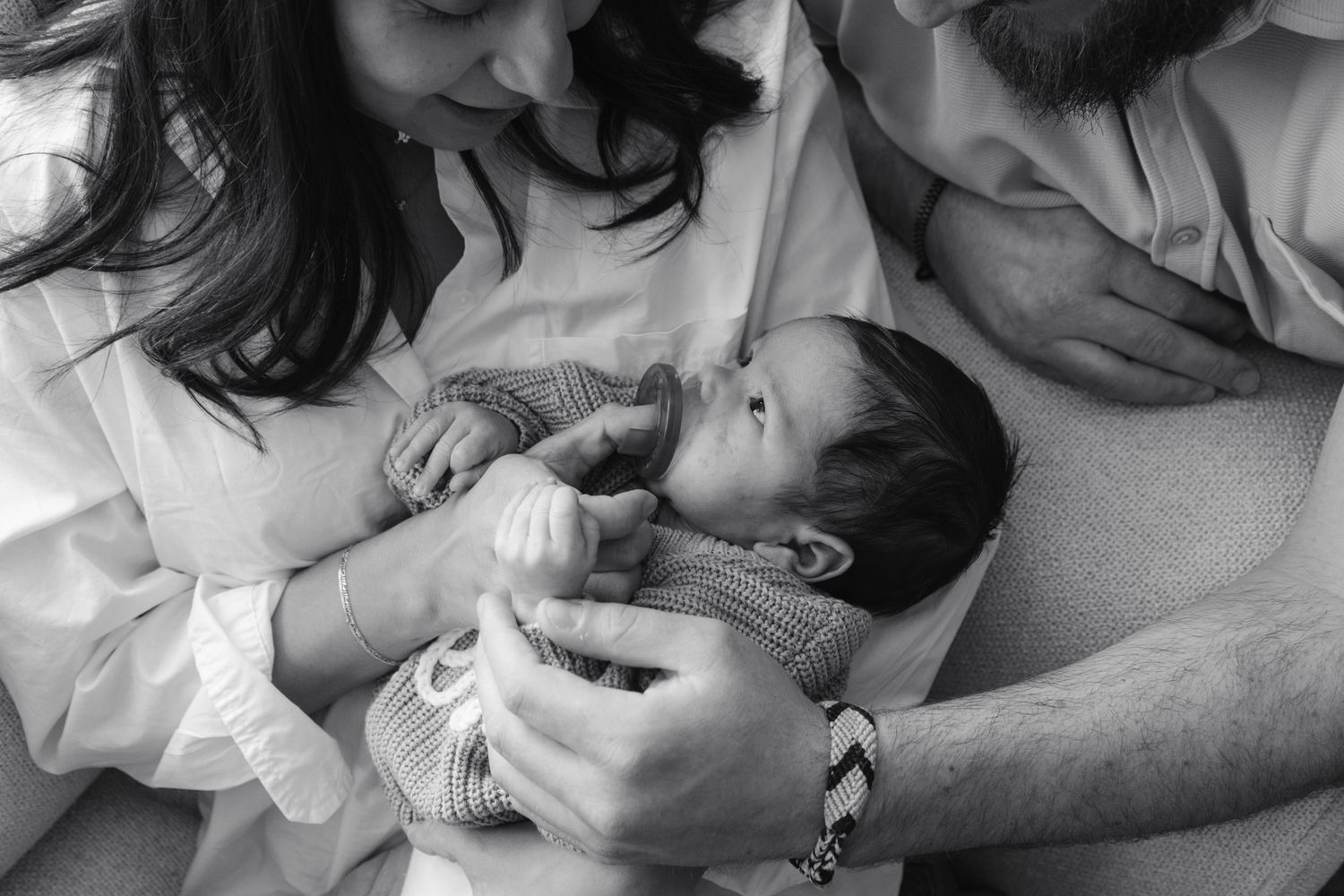 Black and white photo of new parents tenderly holding their newborn baby together.