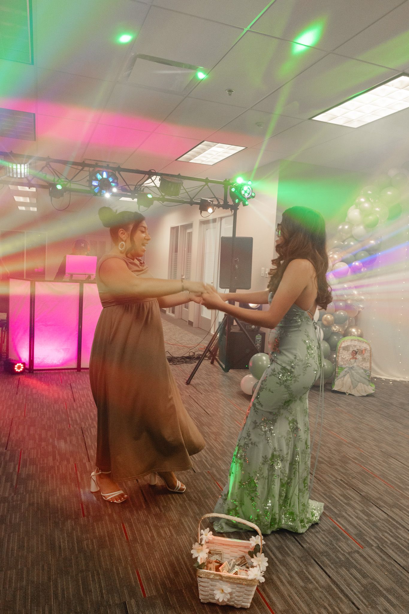 Two women in elegant dresses dancing together at a festive event with colorful stage lighting.