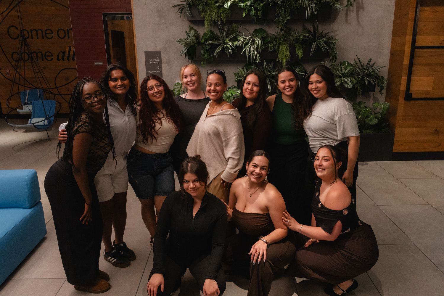 Group of diverse women smiling together indoors near tropical plants and modern decor.
