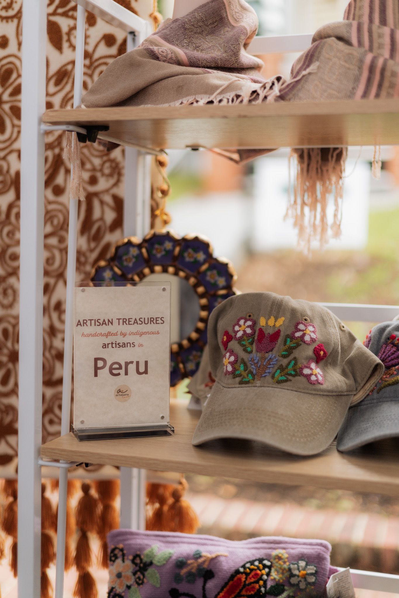 Artisan Treasures display shelf featuring embroidered Peru hat, scarves, and handcrafted goods by indigenous Peruvian artisans.